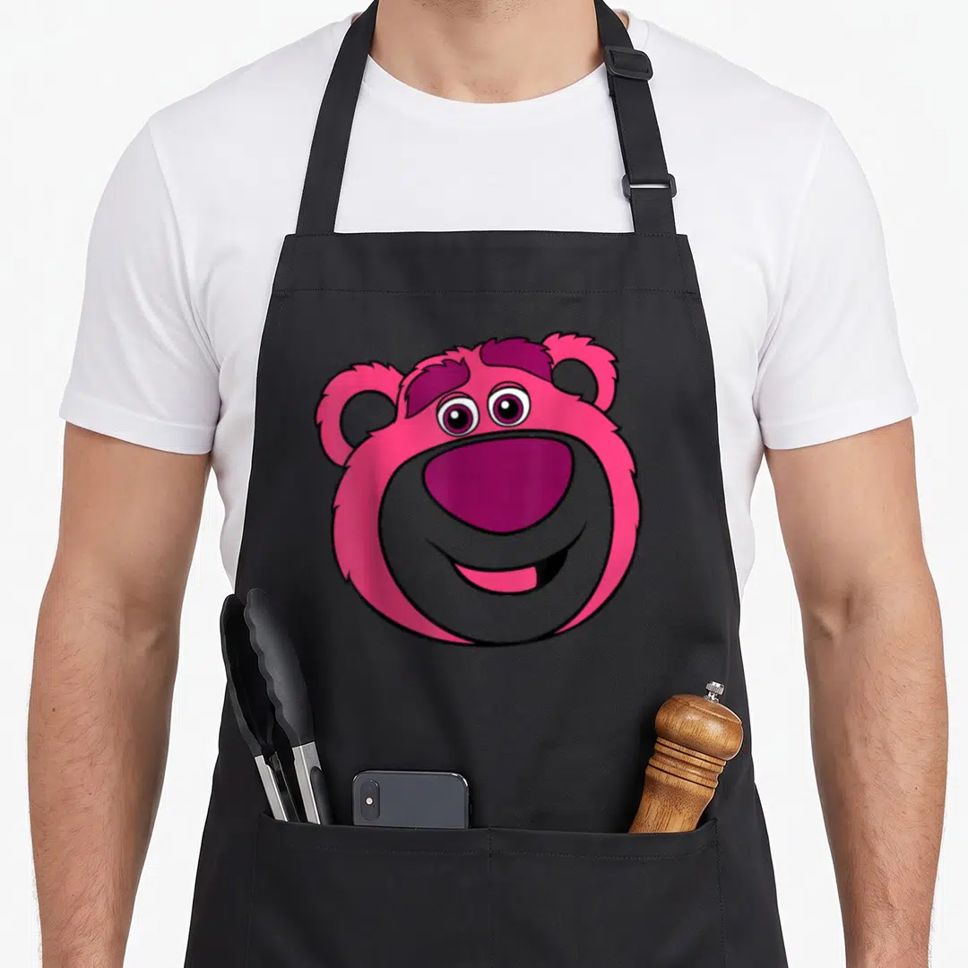 Lotso bear dog breed aprons - Cartoon bear head in pink purple and grey with a smile — shown on a black cotton canvas apron against a white background