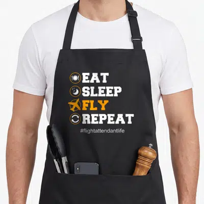 Funny flight attendant problems apron - Stacked EAT SLEEP FLY REPEAT text with plate moon airplane repeat icons — shown on a black cotton canvas apron against a white background