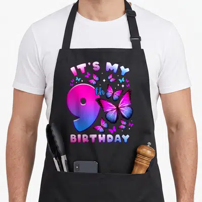 Funny birthday butterfly aprons - Arched IT'S MY 9th BIRTHDAY text with pink blue purple butterflies and stars around — shown on a black cotton canvas apron against a white background
