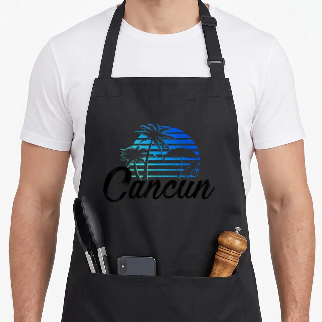 Destination mexico apron - Retro blue gradient sun with stripes behind palm trees and black Cancun script — shown on a black cotton canvas apron against a white background