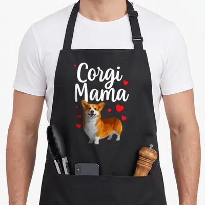 Dog welsh apron - Corgi Mama text above orange white corgi with red hearts — shown on a black cotton canvas apron against a white background