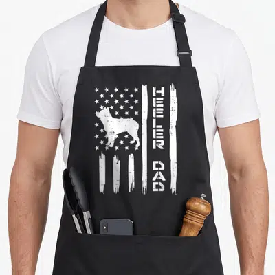 Patriot dog apron - White distressed flag with cattle dog silhouette and stacked heeler dad text on black fabric — shown on a black cotton canvas apron against a white background