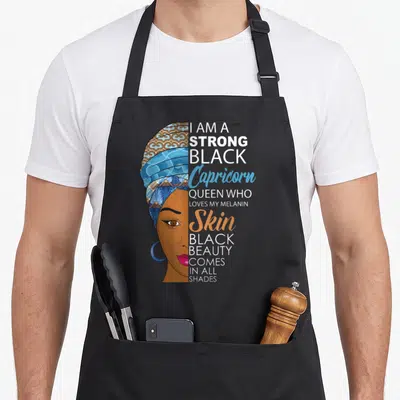 Strong melanin birthday apron - Woman profile in headwrap next to text I am a strong black Capricorn queen loves my — shown on a black cotton canvas apron against a white background