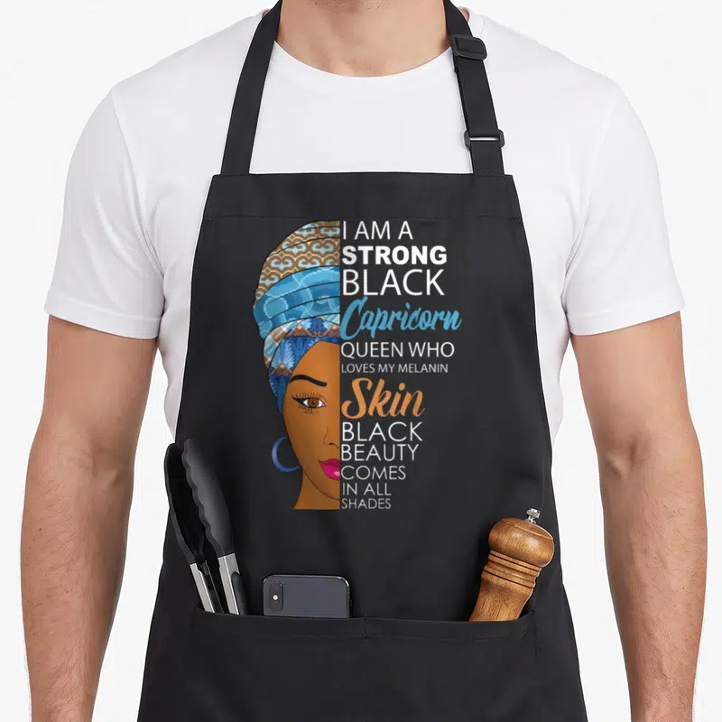 Strong melanin birthday apron - Woman profile in headwrap next to text I am a strong black Capricorn queen loves my — shown on a black cotton canvas apron against a white background