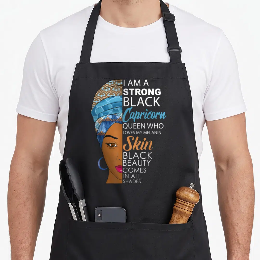 Strong melanin birthday apron - Woman profile in headwrap next to text I am a strong black Capricorn queen loves my — shown on a black cotton canvas apron against a white background