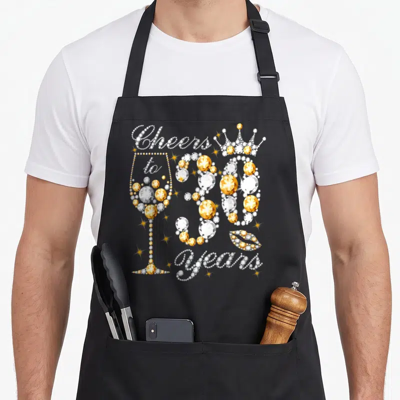30th wine apron - Gold and white rhinestone text Cheers to 30 Years with champagne glass, crown, and lips — shown on a black cotton canvas apron against a white background