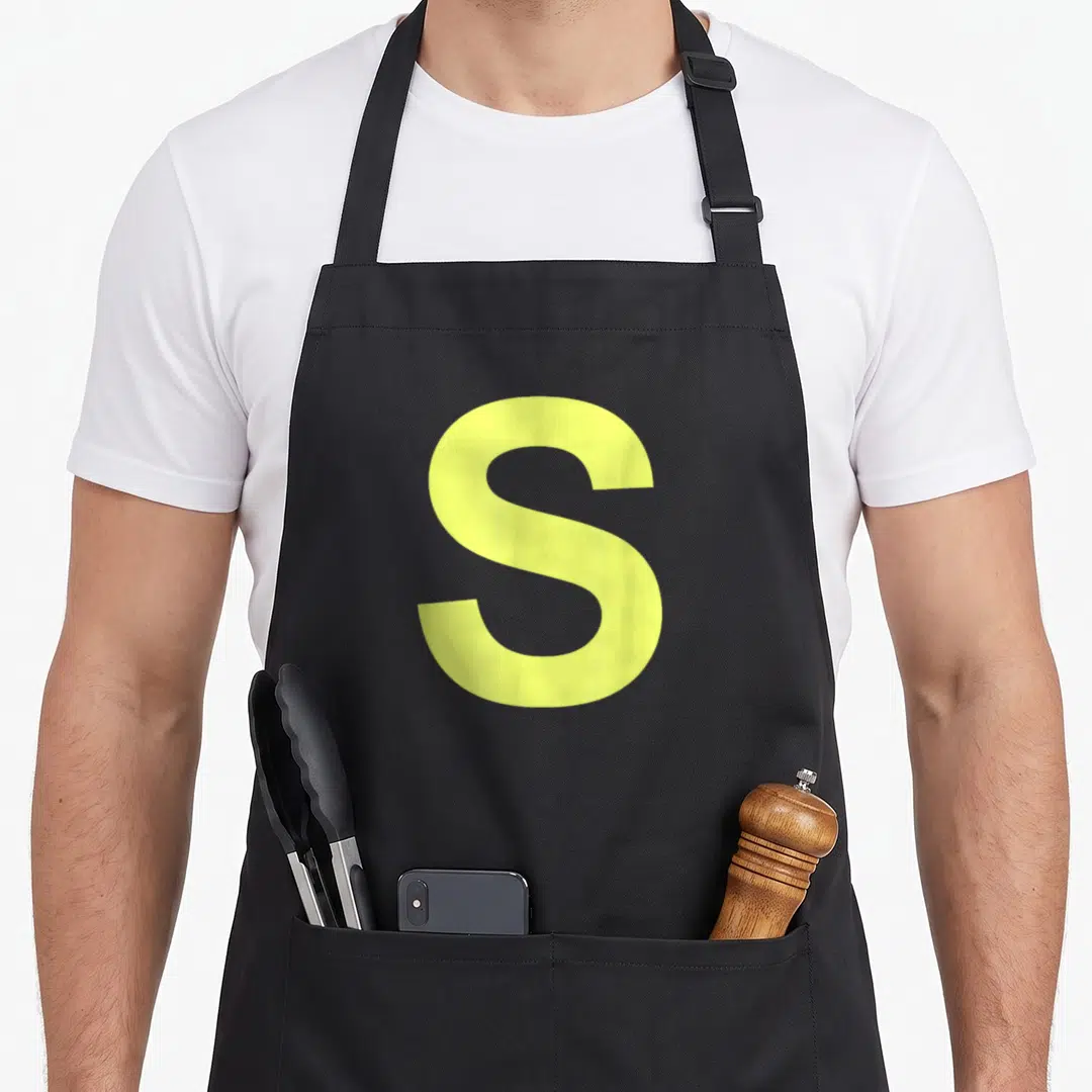 Chipmunk halloween white apron - Large yellow capital letter S on grey background — shown on a black cotton canvas apron against a white background