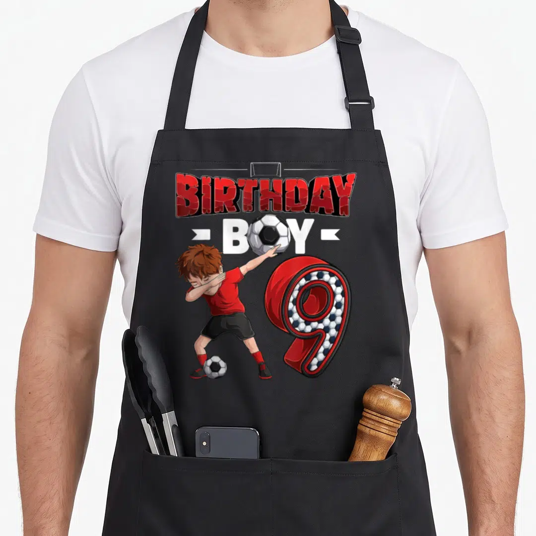 Player 9th birthday apron - Cartoon boy dabbing with soccer ball, red BIRTHDAY BOY text, large number 9 patterned — shown on a black cotton canvas apron against a white background