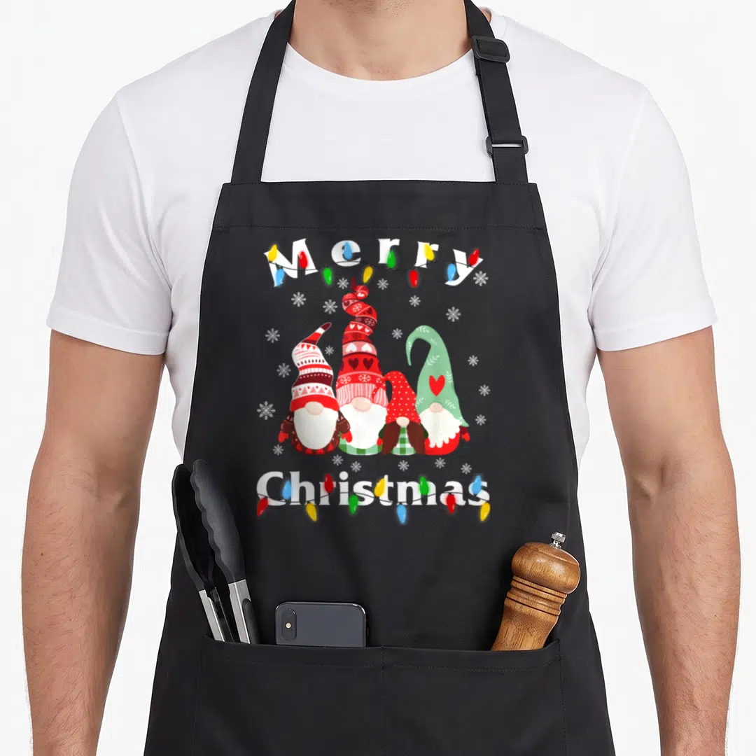 Gnome christmas lights apron - Four gnomes in a row with Merry Christmas text and colorful lights — shown on a black cotton canvas apron against a white background