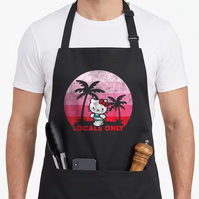 Funny local apron - Hello Kitty inside pink striped circle with palm trees and Locals Only text — shown on a black cotton canvas apron against a white background