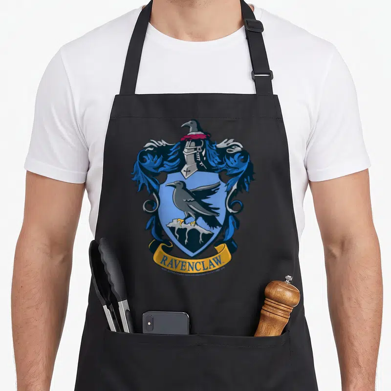 Crest ravenclaw apron - Heraldic shield with raven, helmet, and yellow RAVENCLAW banner in blue and grey — shown on a black cotton canvas apron against a white background