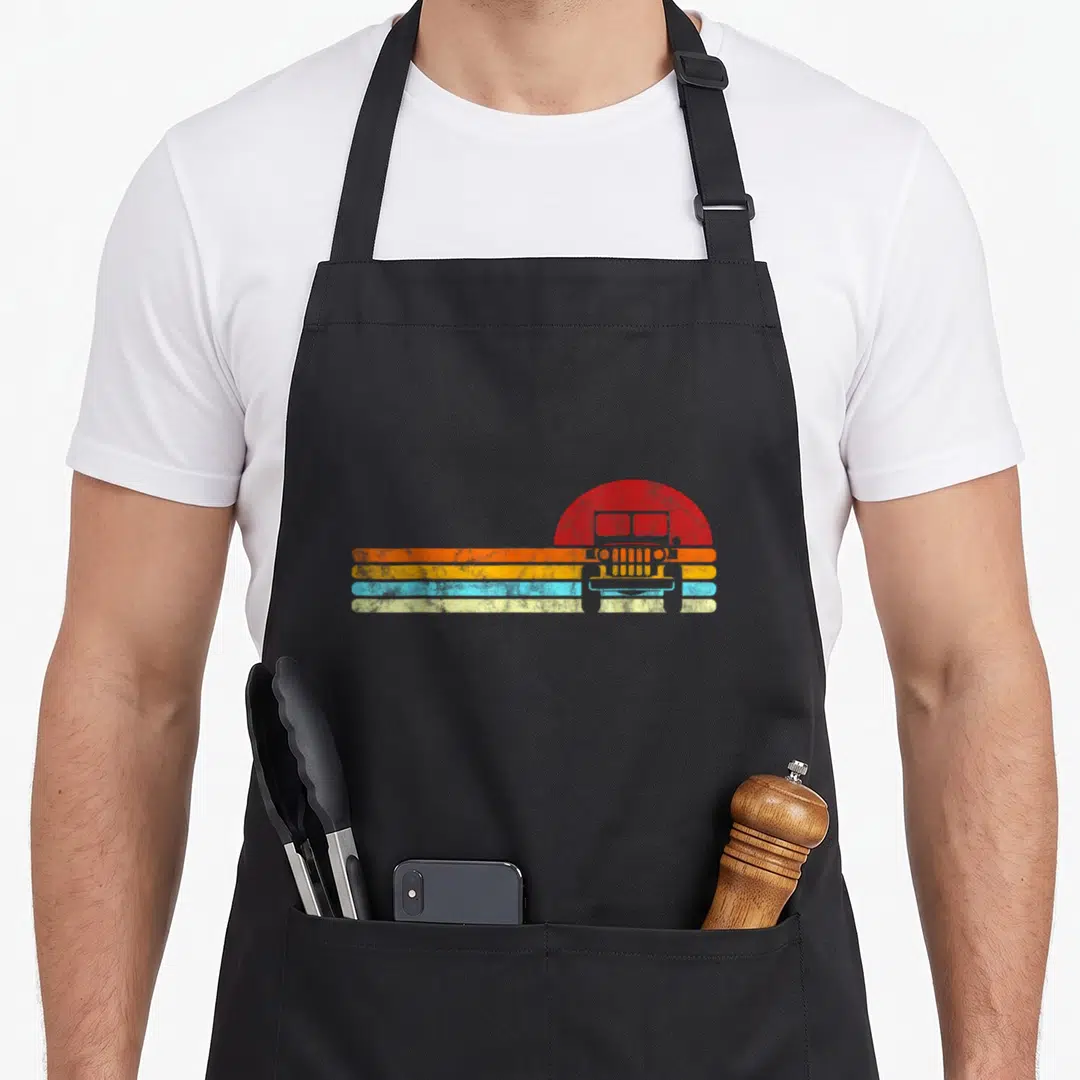 Sunset road apron - Retro jeep silhouette in front of red sun with four horizontal colored stripes — shown on a black cotton canvas apron against a white background