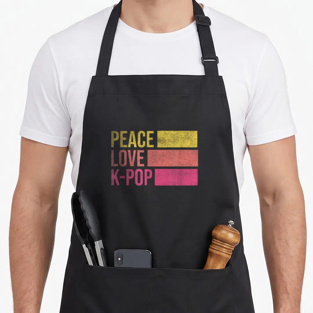 Vintage trend apron - PEACE LOVE K-POP text in yellow coral and pink with matching color blocks — shown on a black cotton canvas apron against a white background