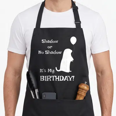 Groundhog 2nd apron - White groundhog silhouette holding balloon with text Shadow or No Shadow It's My BIRTHDAY! — shown on a black cotton canvas apron against a white background