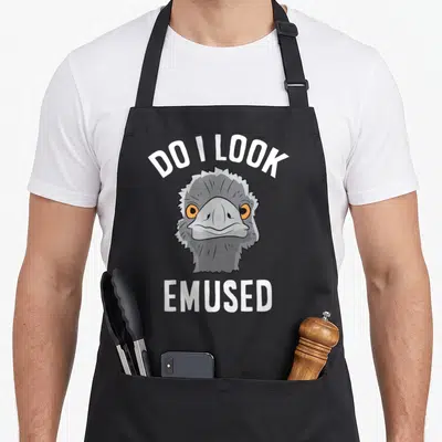 Amused animal apron - Cartoon emu head with orange eyes and white text DO I LOOK EMUSED arched above and straight below — shown on a black cotton canvas apron against a white background