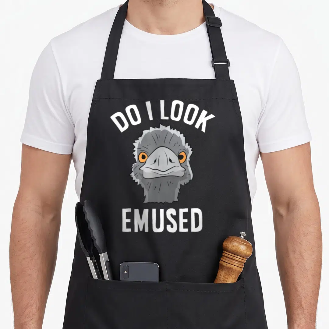 Amused animal apron - Cartoon emu head with orange eyes and white text DO I LOOK EMUSED arched above and straight below — shown on a black cotton canvas apron against a white background