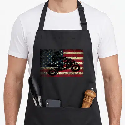 Brap american flag apron - Black ATV rider silhouette on distressed red white blue USA flag graphic — shown on a black cotton canvas apron against a white background