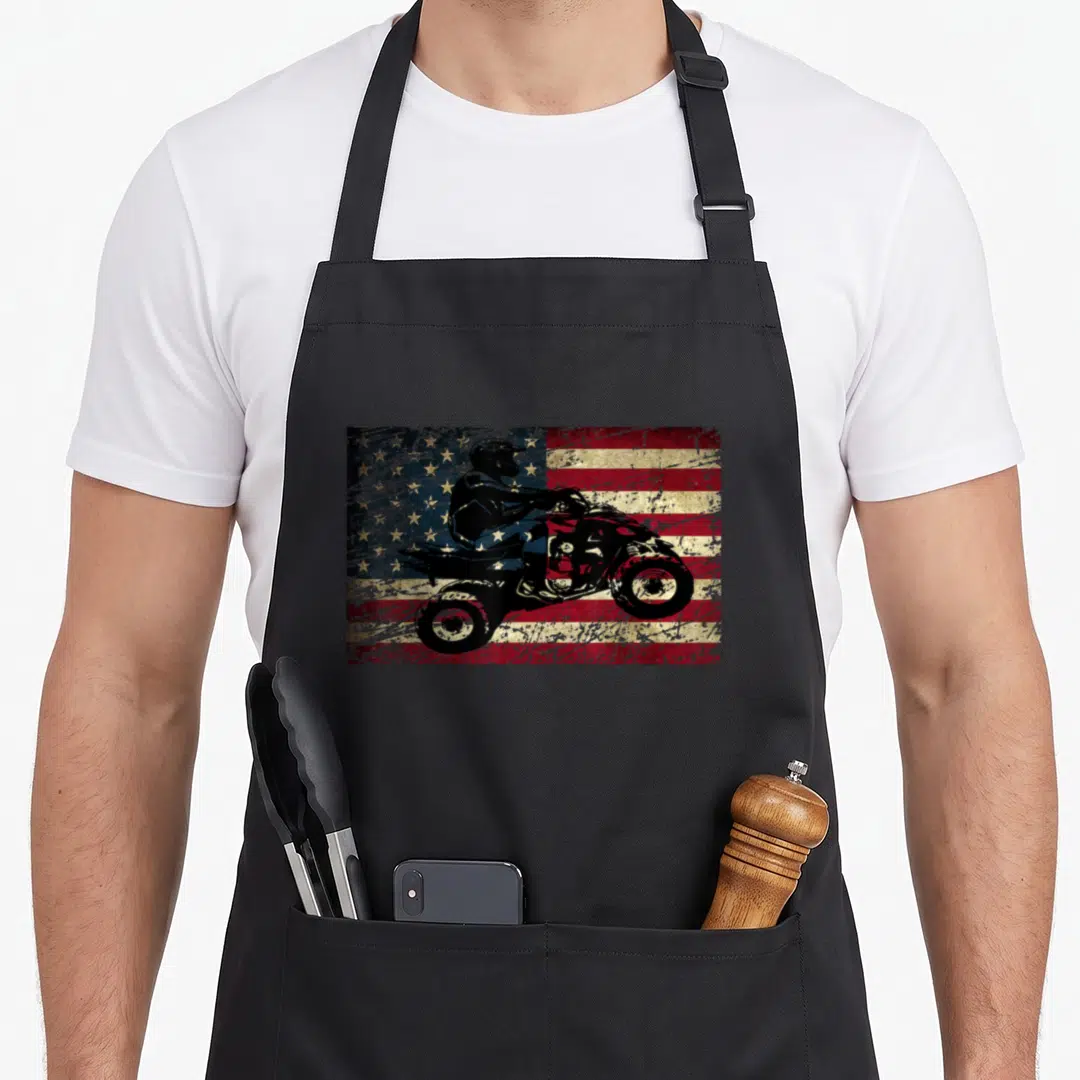 Brap american flag apron - Black ATV rider silhouette on distressed red white blue USA flag graphic — shown on a black cotton canvas apron against a white background
