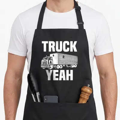 Yeah semi truck apron - White TRUCK and YEAH text framing a vintage cab-over semi truck illustration — shown on a black cotton canvas apron against a white background