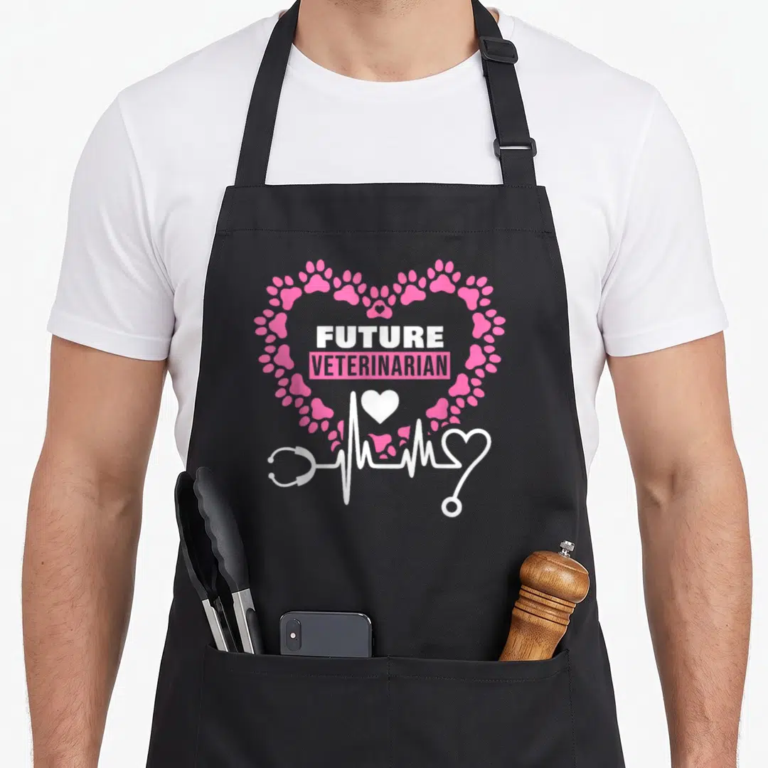 Future veterinarian doctor apron - Pink paw print heart enclosing FUTURE VETERINARIAN text with white stethoscope — shown on a black cotton canvas apron against a white background