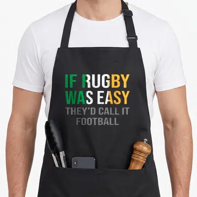 Rugby irish aprons - IF RUGBY WAS EASY THEY'D ALL PLAY FOOTBALL text in green white orange grey block letters — shown on a black cotton canvas apron against a white background