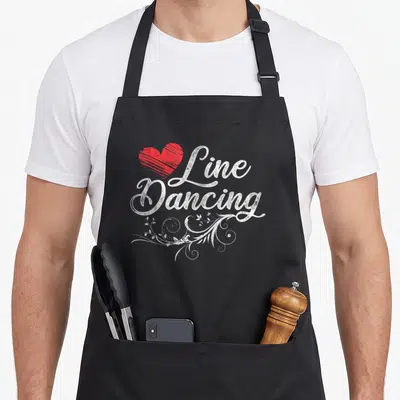 Dance line apron - Red heart beside white Line Dancing text with floral swirls — shown on a black cotton canvas apron against a white background