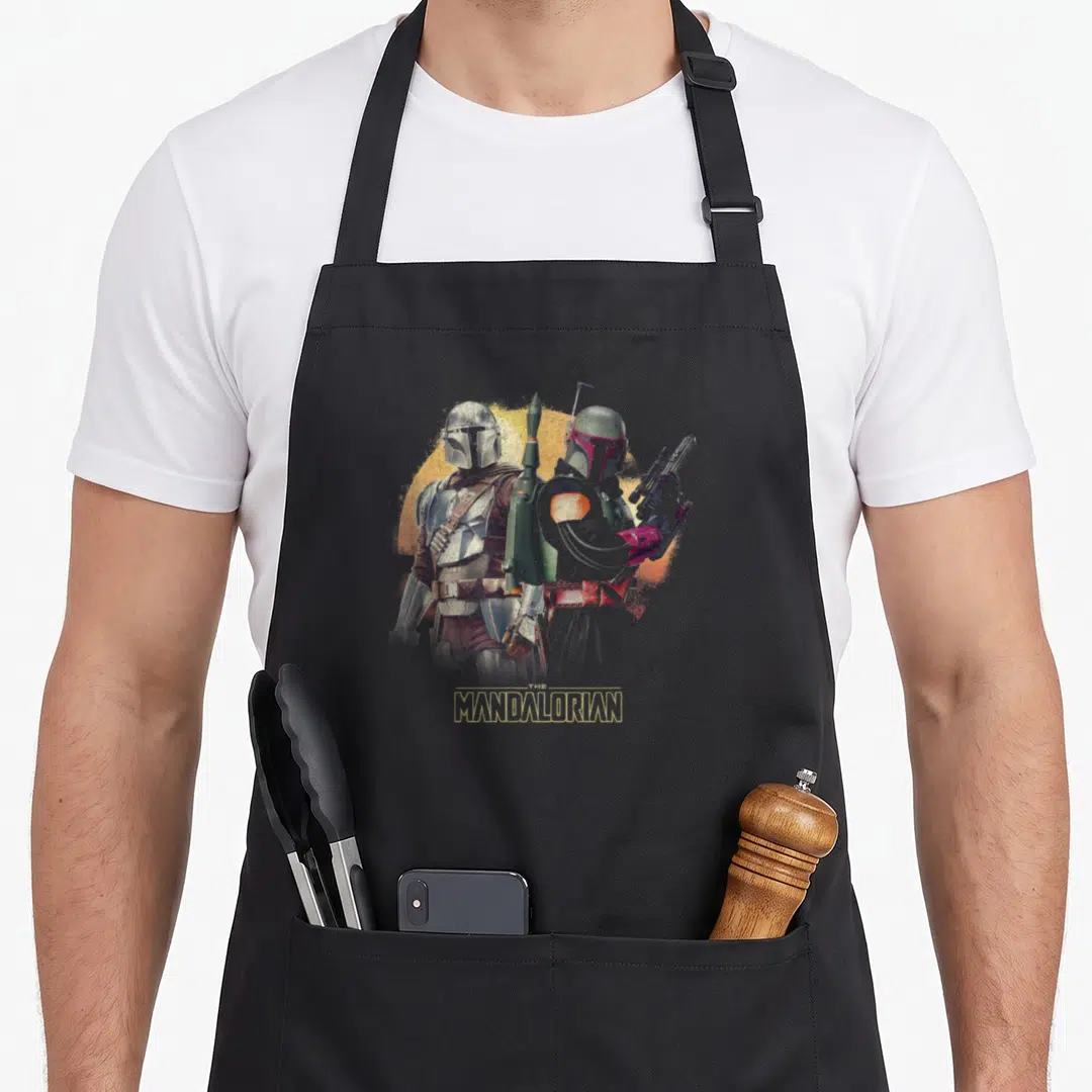 R15 boba apron - Two armored figures standing side-by-side before orange circle with gold text — shown on a black cotton canvas apron against a white background