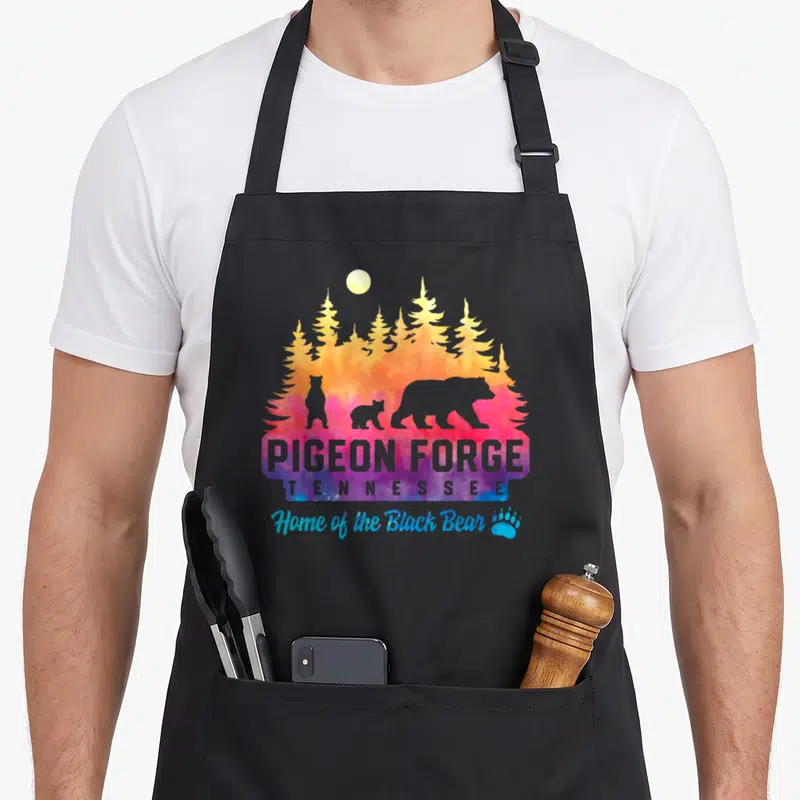 Pigeon tie-dye apron - Pigeon Forge Tennessee bear silhouettes watercolor moon pine trees paw print — shown on a black cotton canvas apron against a white background