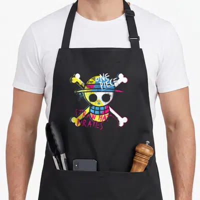 Straw novelty apron - Distressed skull and crossbones with One Piece Straw Hat Pirates text in yellow, blue, pink — shown on a black cotton canvas apron against a white background