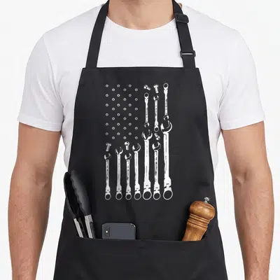 Mechanic american flag apron - White nuts and wrenches arranged in a flag pattern on grey background — shown on a black cotton canvas apron against a white background
