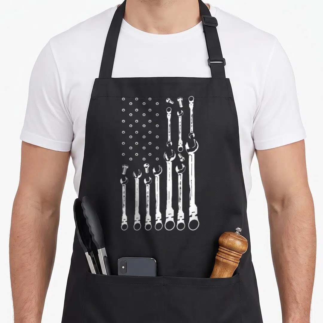 Mechanic american flag apron - White nuts and wrenches arranged in a flag pattern on grey background — shown on a black cotton canvas apron against a white background