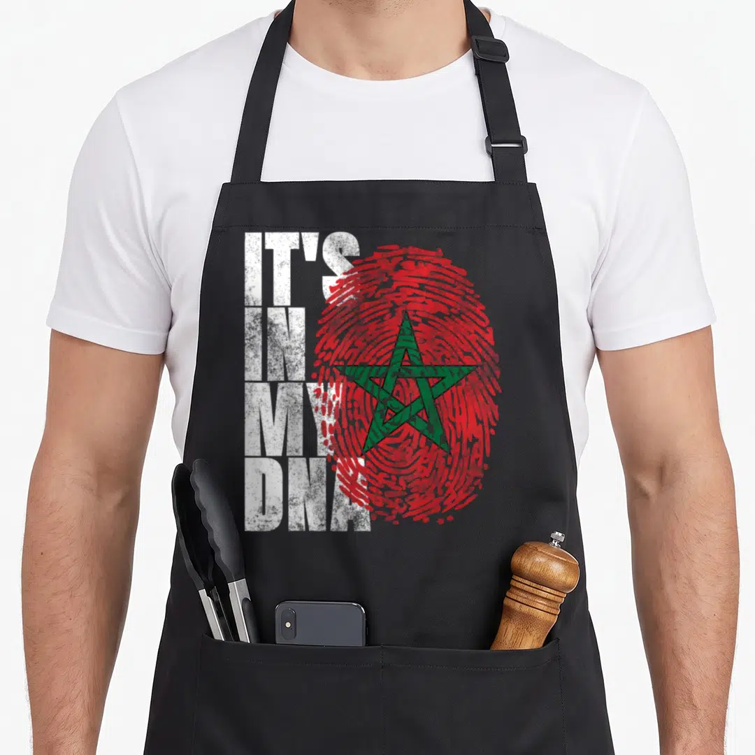 Dna african apron - IT'S IN MY DNA text over red fingerprint with green star — shown on a black cotton canvas apron against a white background