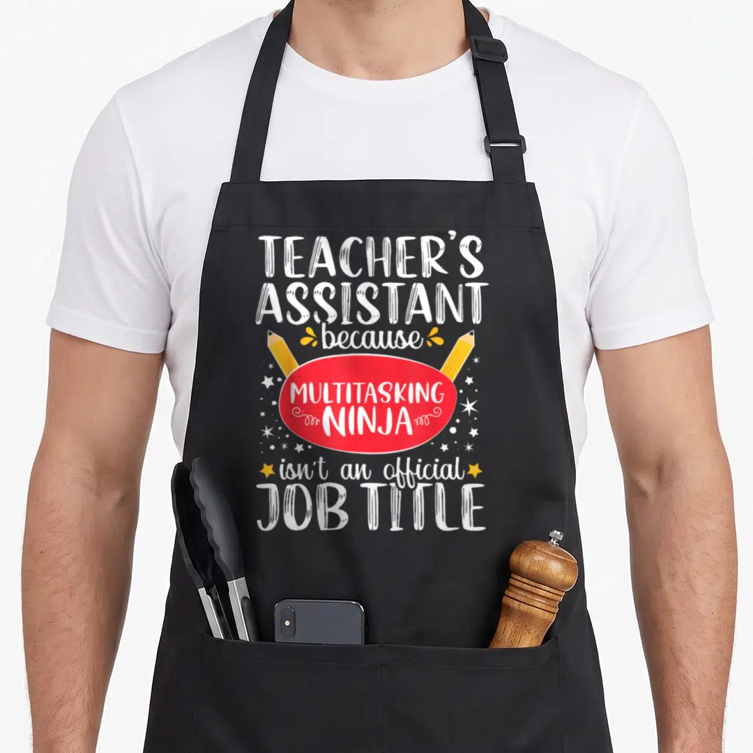Assistant teaching teacher apron - Stacked white text reading Teacher Assistant Multitasking Ninja with red oval — shown on a black cotton canvas apron against a white background