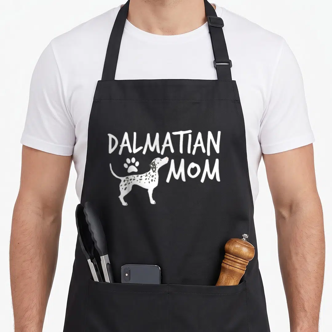 Dalmatian puppy dog apron - White cartoon dalmatian with black spots and paw print next to DALMATIAN MOM text — shown on a black cotton canvas apron against a white background
