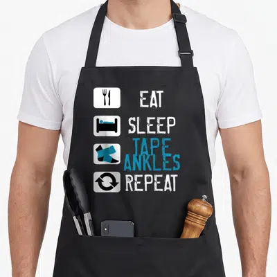 Trainer funny athletic apron - EAT SLEEP TAPE ANKLES REPEAT text with fork knife bed tape and recycle icons in white — shown on a black cotton canvas apron against a white background