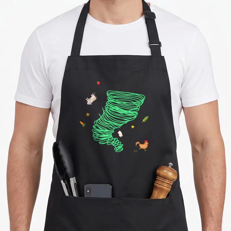 Tornado hurricane ridge apron - Green spiral tornado with cartoon cow pig chicken carrot cheese tomato and leaf — shown on a black cotton canvas apron against a white background