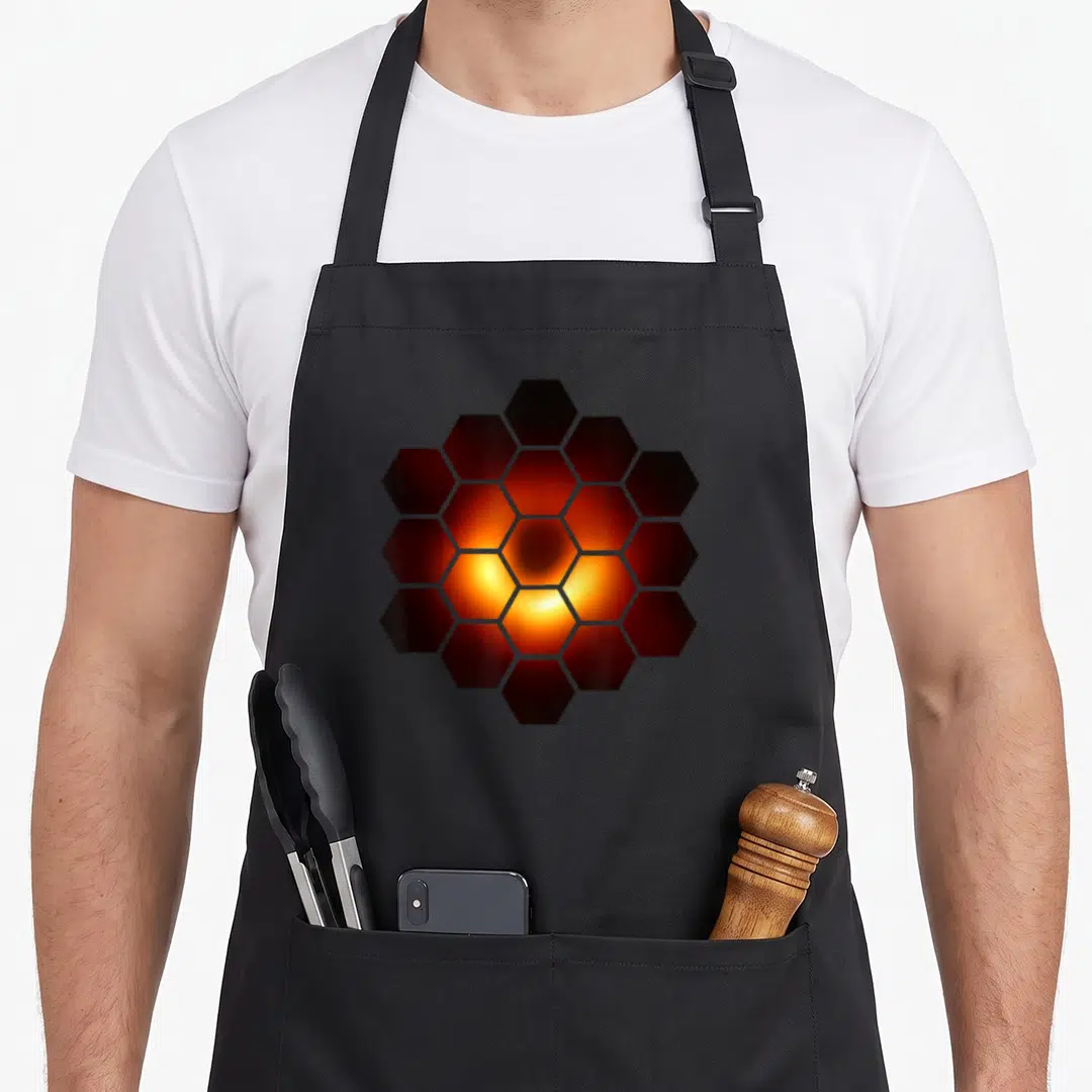 Messier black hole apron - Hexagon cluster with orange yellow glow fading to black edges — shown on a black cotton canvas apron against a white background