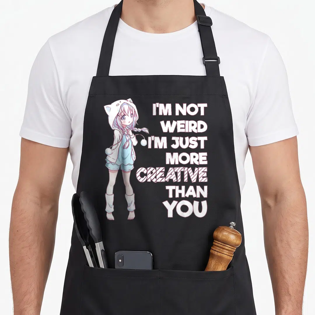 Weird creative apron - Anime girl in white hoodie beside stacked text reading I'M NOT WEIRD I'M JUST MORE CREATIVE THAN — shown on a black cotton canvas apron against a white background