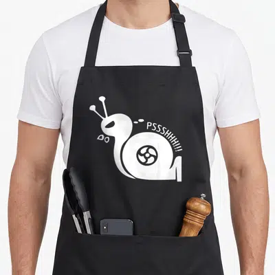 Pshh racing apron - White snail silhouette with turbo symbol and curved PSSSHHHH text — shown on a black cotton canvas apron against a white background