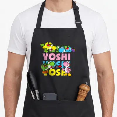 Icon pastel aprons - Four colored Yoshis surrounding stacked YOSHI text in yellow blue pink green cartoon style — shown on a black cotton canvas apron against a white background