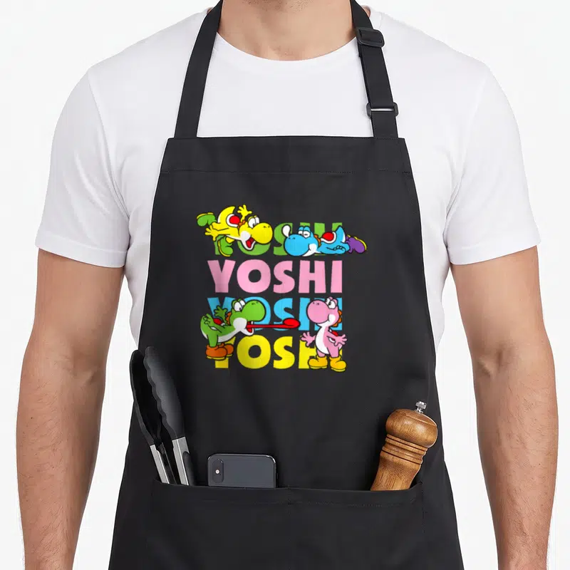 Icon pastel aprons - Four colored Yoshis surrounding stacked YOSHI text in yellow blue pink green cartoon style — shown on a black cotton canvas apron against a white background