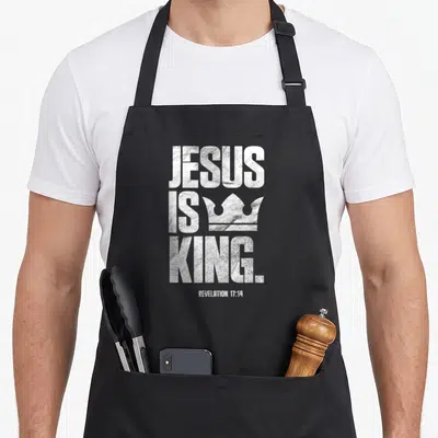 Scripture king of the grill apron - Distressed white JESUS IS KING text with crown and Revelation 17:14 reference — shown on a black cotton canvas apron against a white background