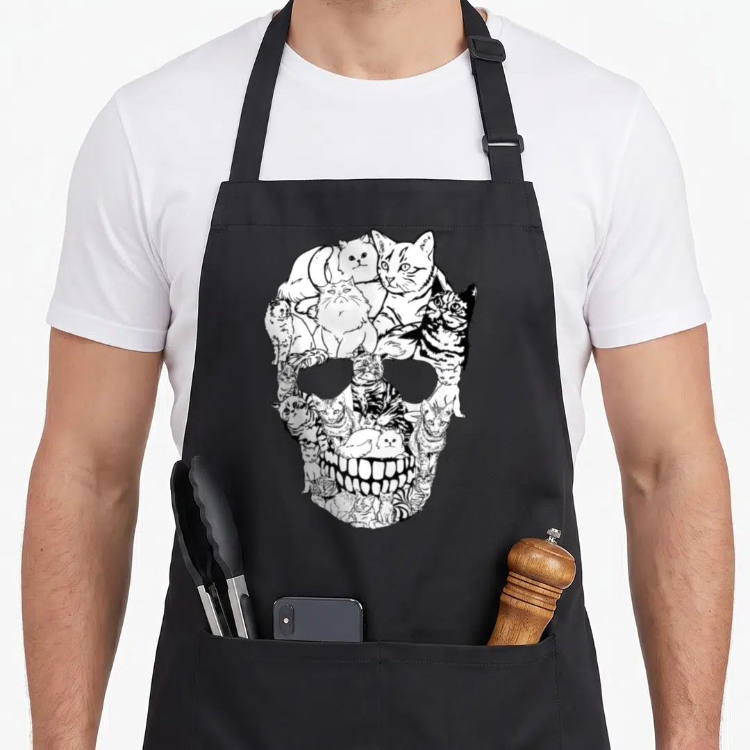 Cat skeleton apron - White line art cats arranged to form a skull shape on black background — shown on a black cotton canvas apron against a white background
