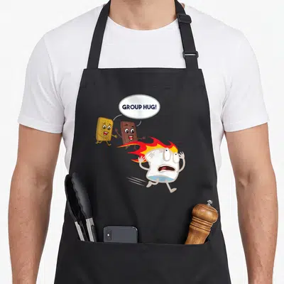 Smore camping apron - Panicked marshmallow running from chocolate and graham cracker with group hug text — shown on a black cotton canvas apron against a white background