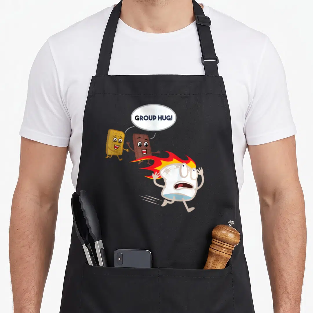 Smore camping apron - Panicked marshmallow running from chocolate and graham cracker with group hug text — shown on a black cotton canvas apron against a white background