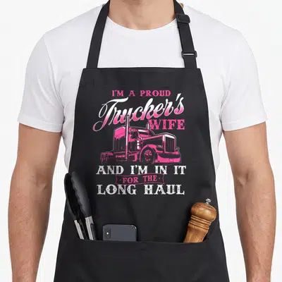 Proud semi truck apron - Pink semi-truck illustration surrounded by stacked white and pink text reading I'm A Proud — shown on a black cotton canvas apron against a white background