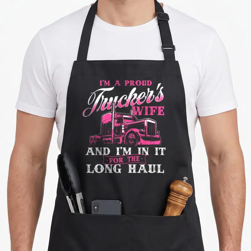 Proud semi truck apron - Pink semi-truck illustration surrounded by stacked white and pink text reading I'm A Proud — shown on a black cotton canvas apron against a white background