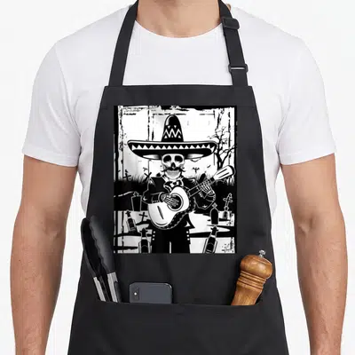 Mariachi skeleton apron - Black and white line art of a skeleton in a sombrero playing guitar among tombstones — shown on a black cotton canvas apron against a white background