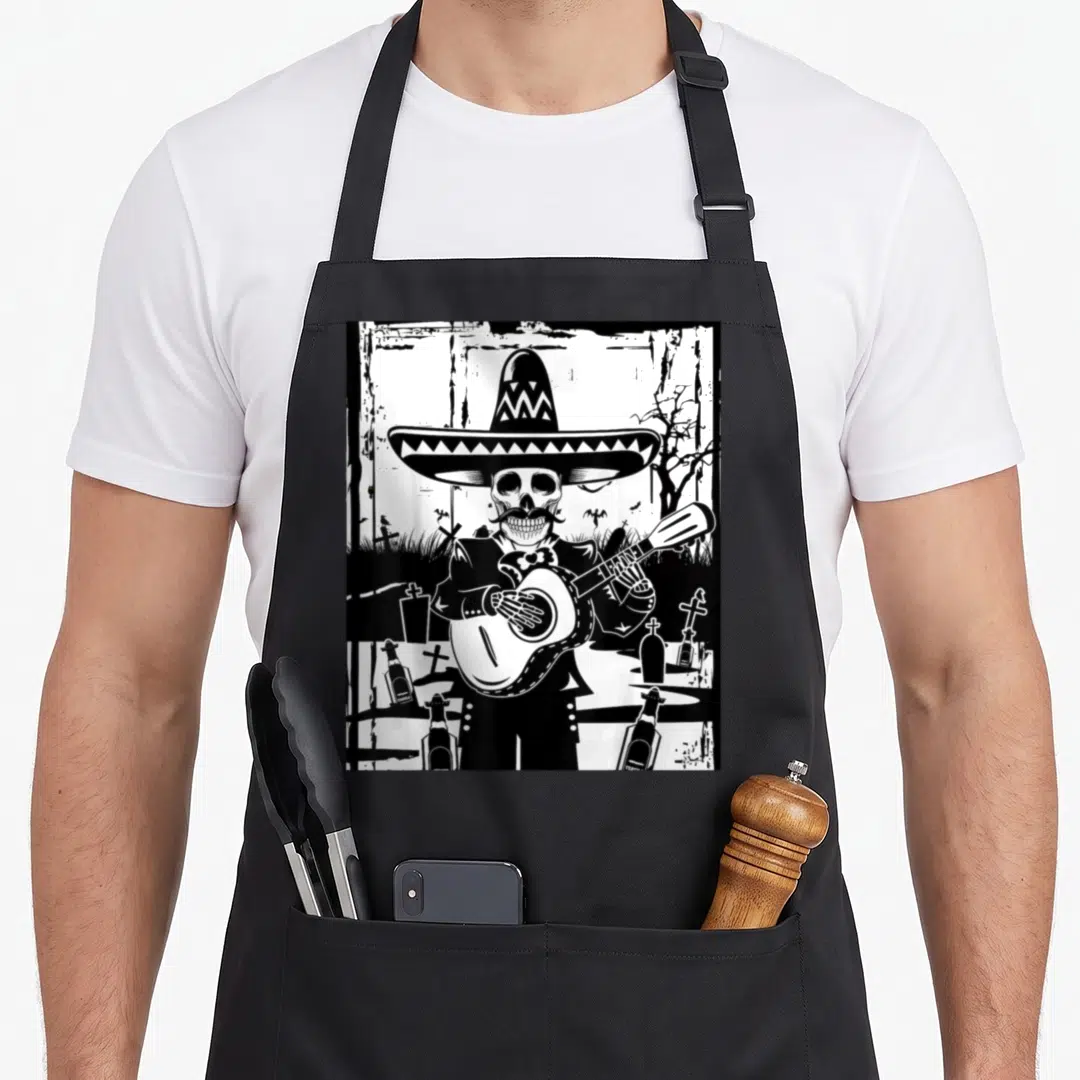 Mariachi skeleton apron - Black and white line art of a skeleton in a sombrero playing guitar among tombstones — shown on a black cotton canvas apron against a white background