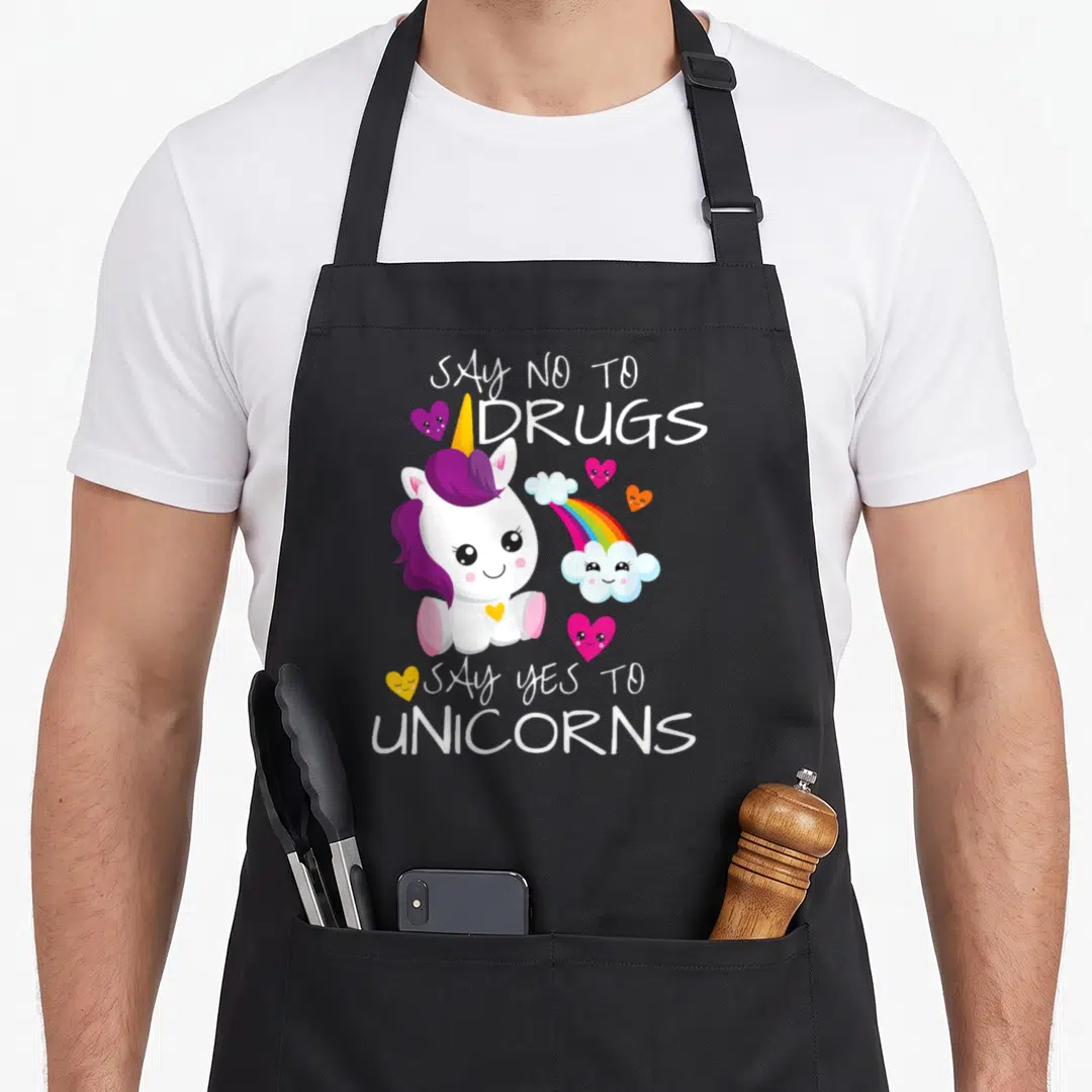 Week unicorn apron - Cartoon white unicorn with purple mane, rainbow cloud, and hearts surrounding text saying say no — shown on a black cotton canvas apron against a white background